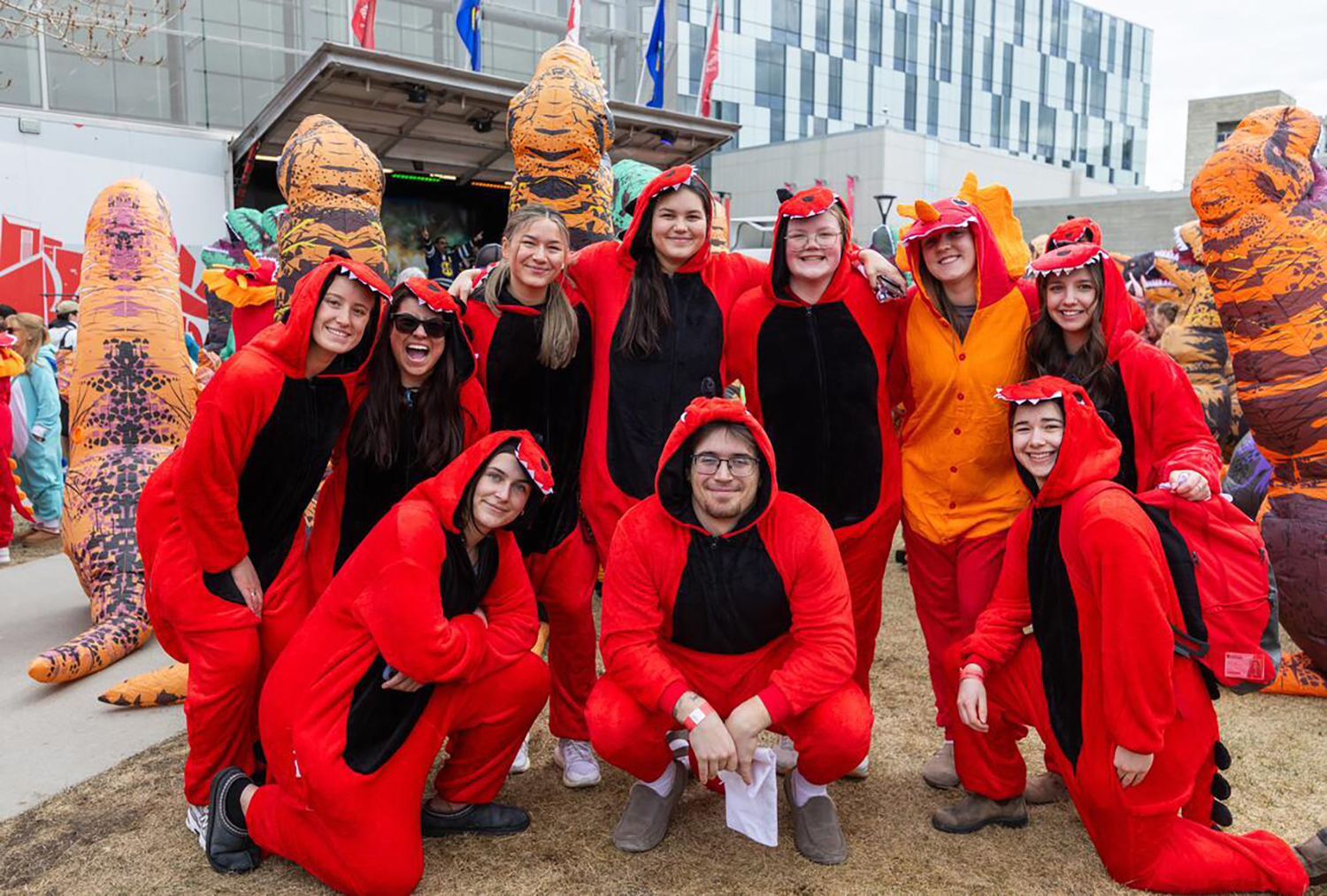 Ten people in nearly identical red dinosaur costumes pose together for a photo.