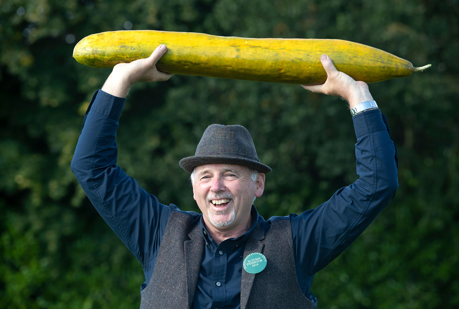 Graham Barratt poses while holding a large cucumber over his head.