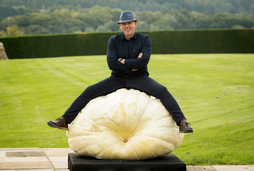 Graham Barratt sits on a giant white pumpkin and smiles.