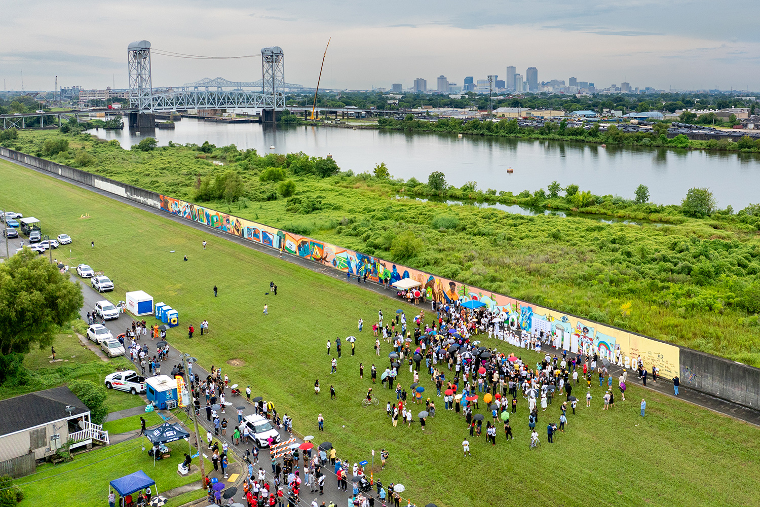 Overhead view of a crowd gathering on a grassy area with the Mississippi River and the New Orleans skyline in the background.