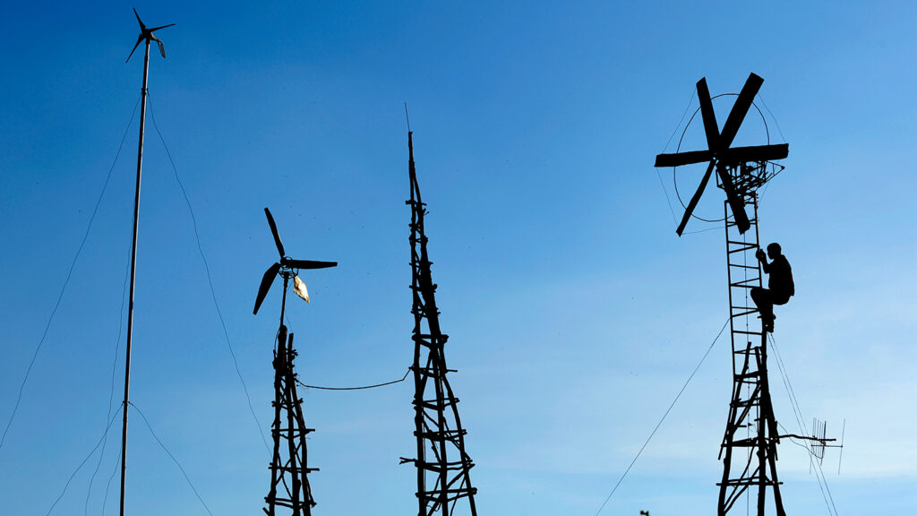 The silhouette of a young man is near the top of one of three windmills.
