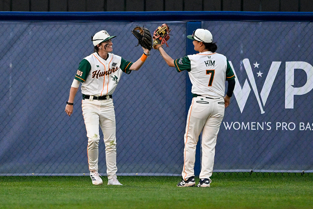 Gabrielle Haas and Hyeonah Kim smile and high five with their baseball gloves.