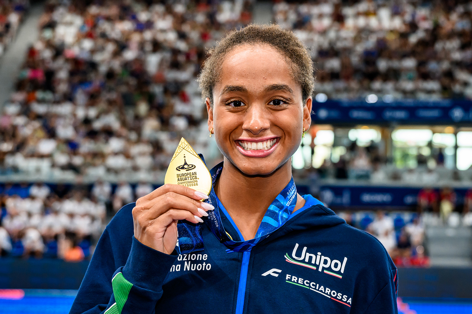 Sara Curtis smiles and holds up a medal that says European Aquatics.