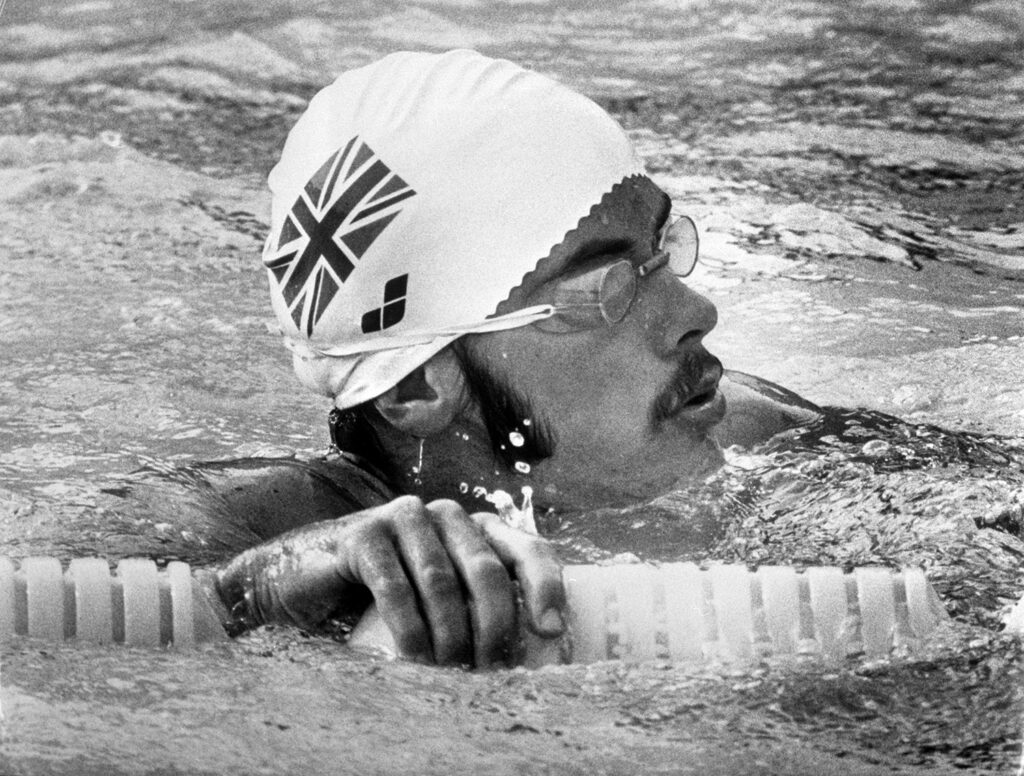 A young David Wilkie is in a pool wearing a swimming cap and goggles.