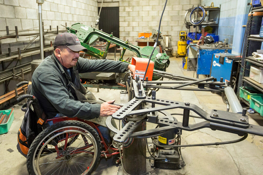A man who uses a wheelchair operates equipment in a workshop.
