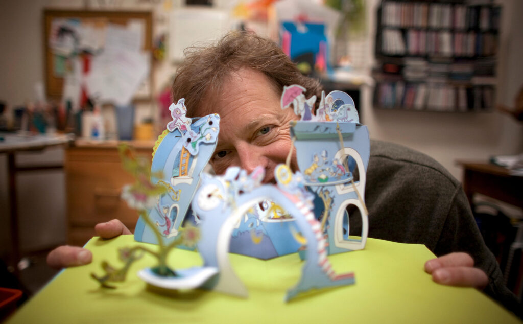 David A. Carter smiles and poses with a pop-up book he designed.