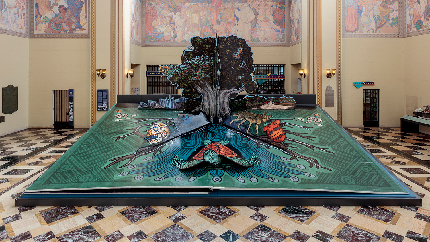 A tree emerges from the pages of a large pop-up book, which is open inside a room with painted walls and ceilings.