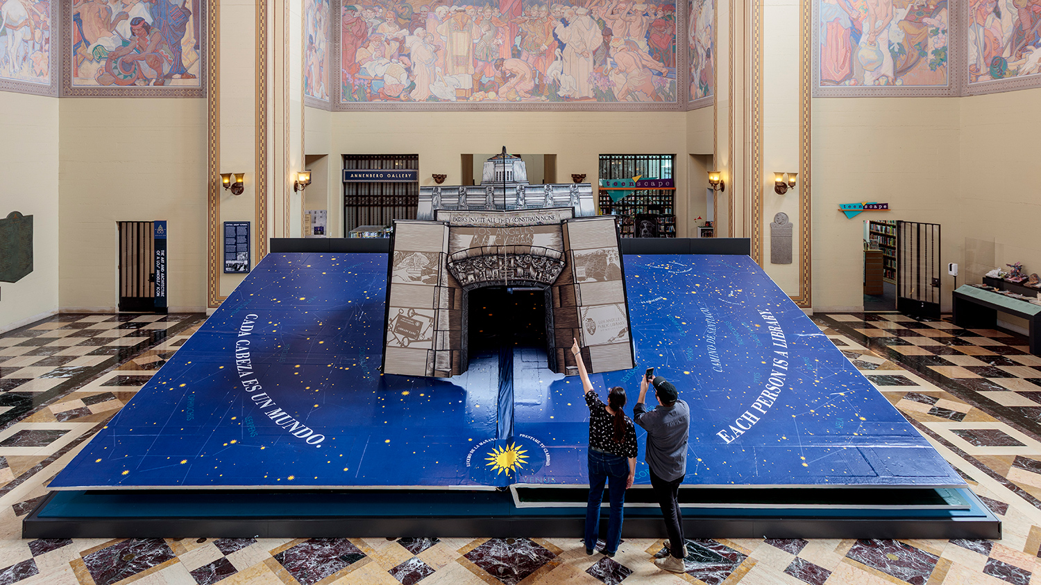 A person points at a giant, open pop-up book as another person takes a photo.