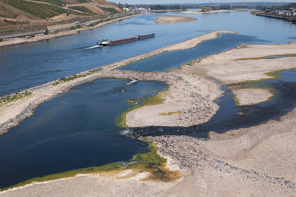 An overhead view of a river with a boat on it shows many exposed patches of the riverbed.