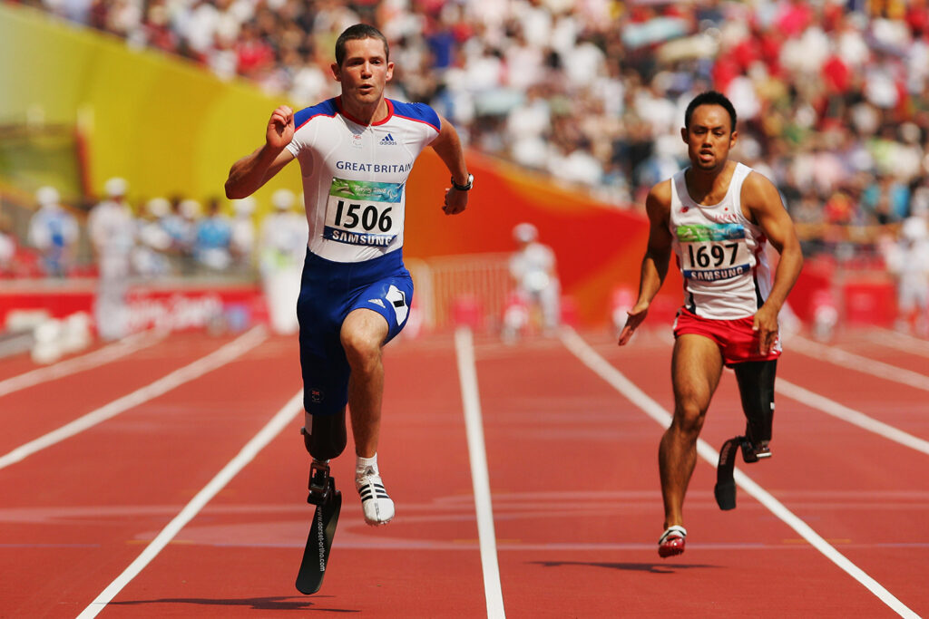 John McFall and Atsushi Yamamoto run on a track with a crowd in the stands behind them.