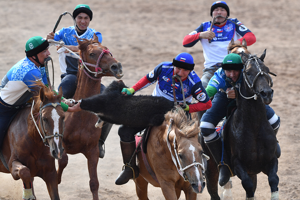 Two men on horseback try to get a sheepskin as three other horseback riders ride nearby.