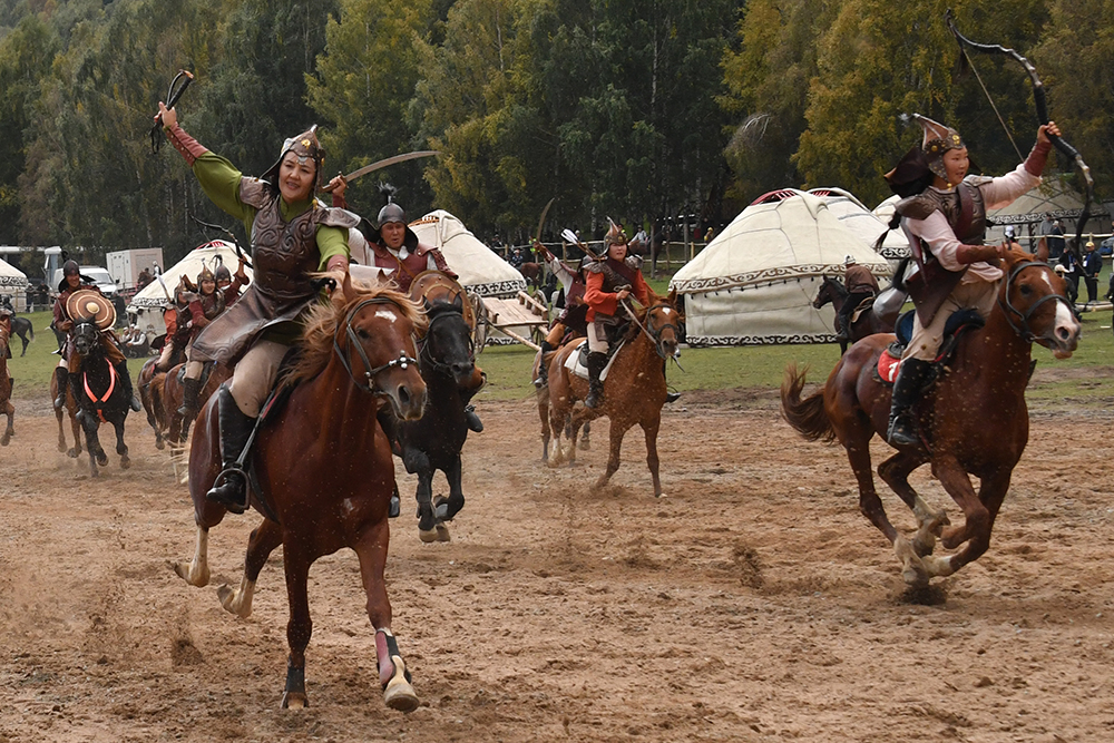 Horseback riders wear traditional clothing and hold up weapons such as bows and swords.