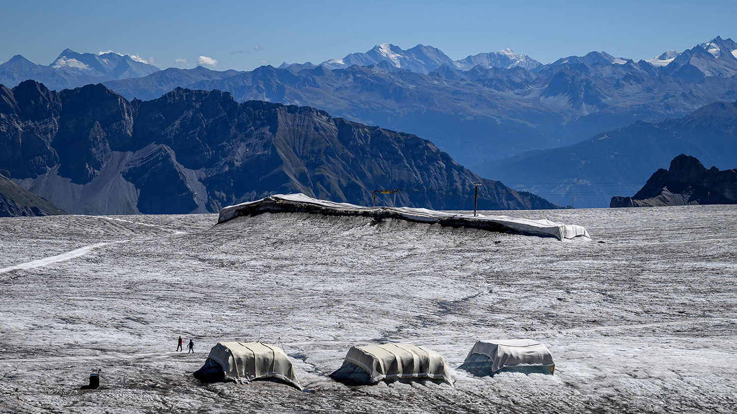 Two large pieces of glacier ice are covered with sheep’s wool and a third is covered by synthetic material in front of a mountain background.