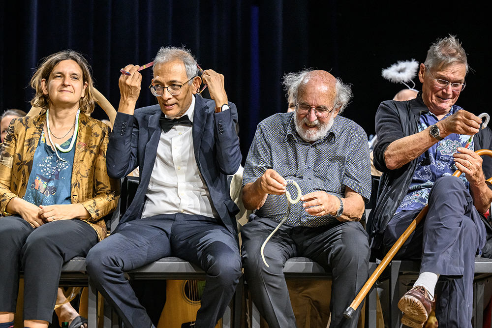Four people are seated on stage and playing with or holding fake snakes.