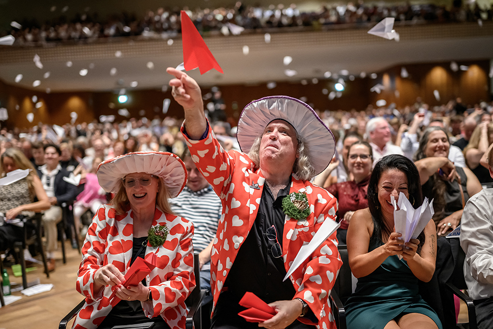Audience members smile as they throw paper airplanes.