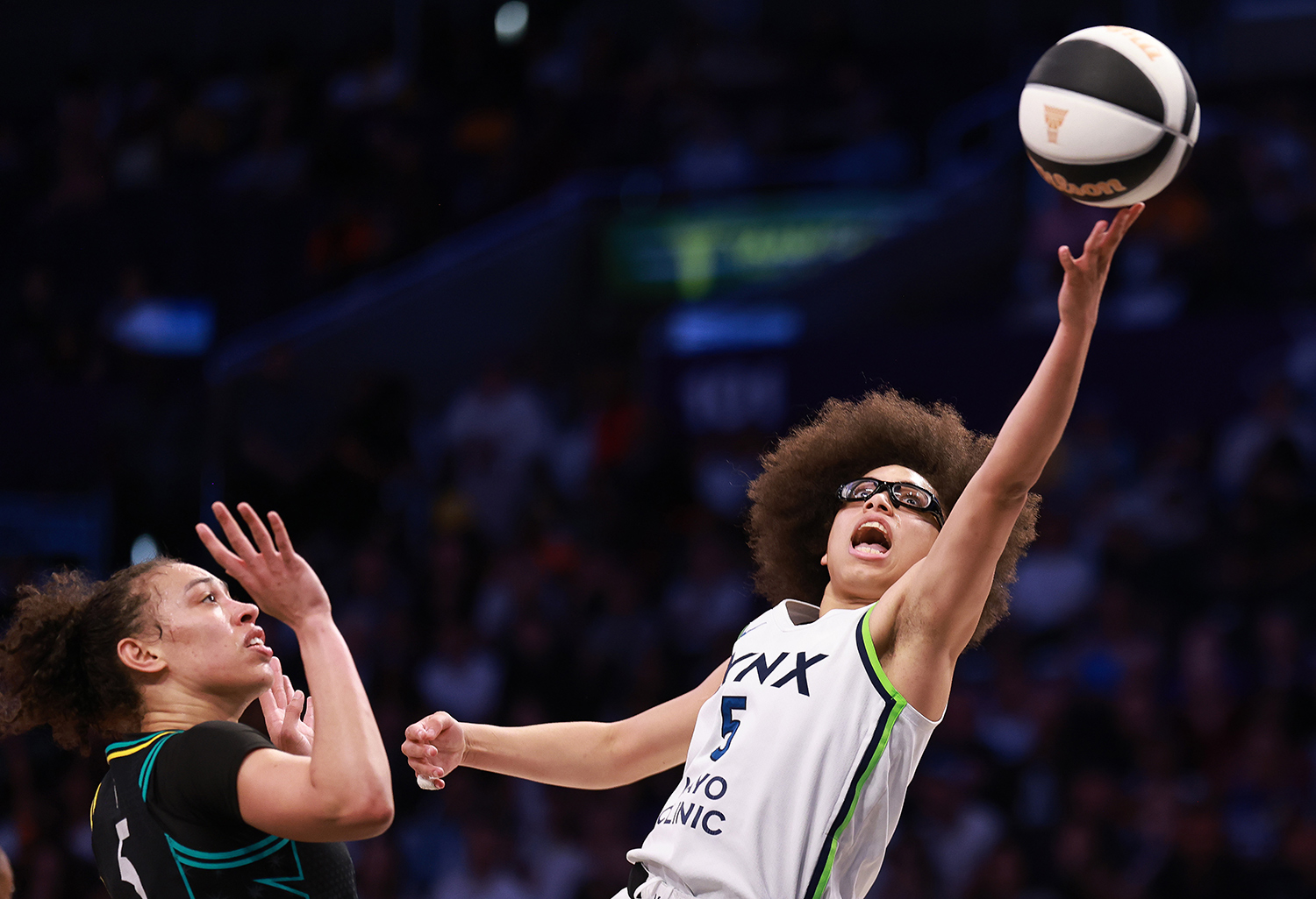 Olivia Miles is in the air with her left arm reaching toward the ball as Dearica Hamby has both of her palms raised.