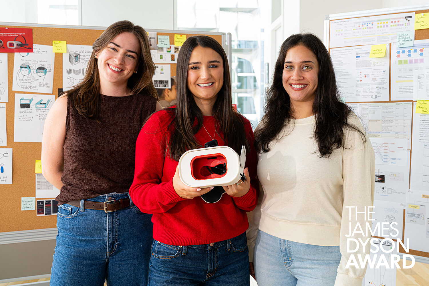 Three young women stand and pose together and the woman in the middle holds the Rumble Rims headset.