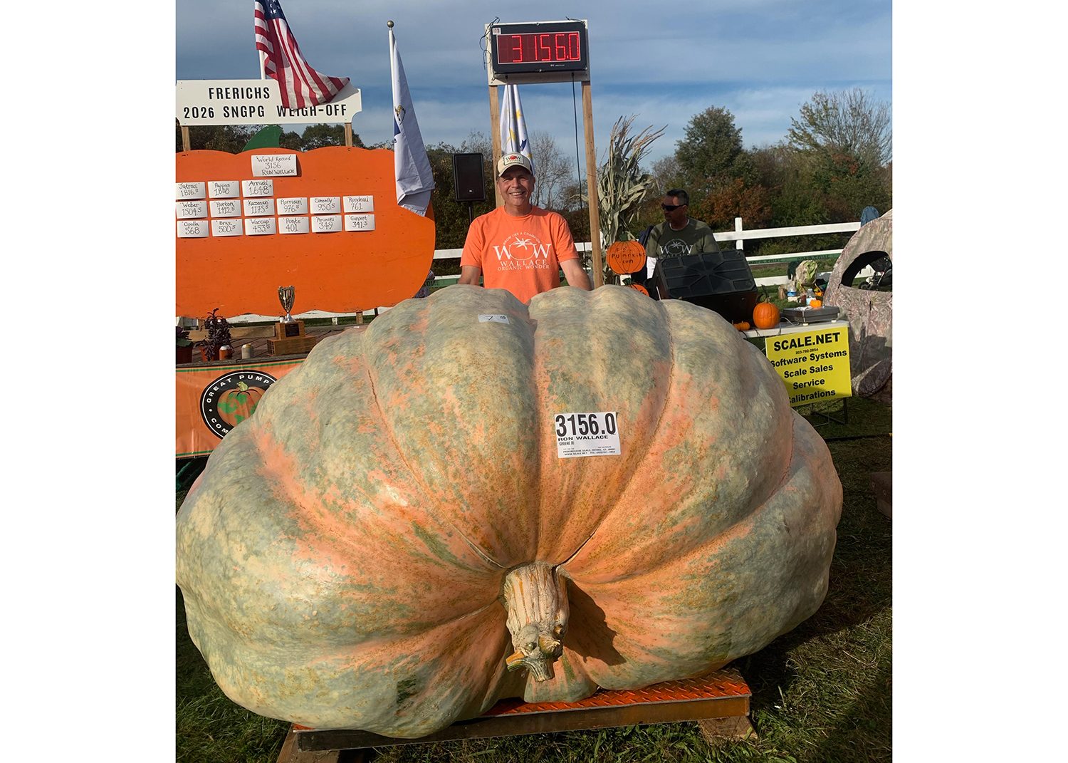 Ron Wallace stands behind a large pumpkin that is on a scale that says it weighs 3,156 pounds.