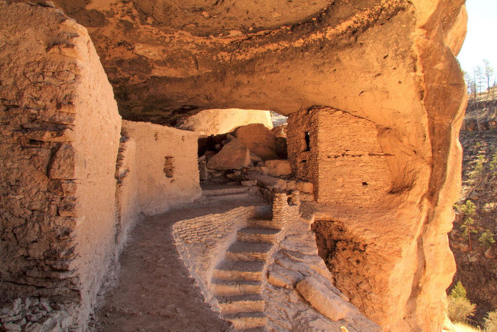 A stone and clay structure, including a staircase, is built on the side of a cliff.