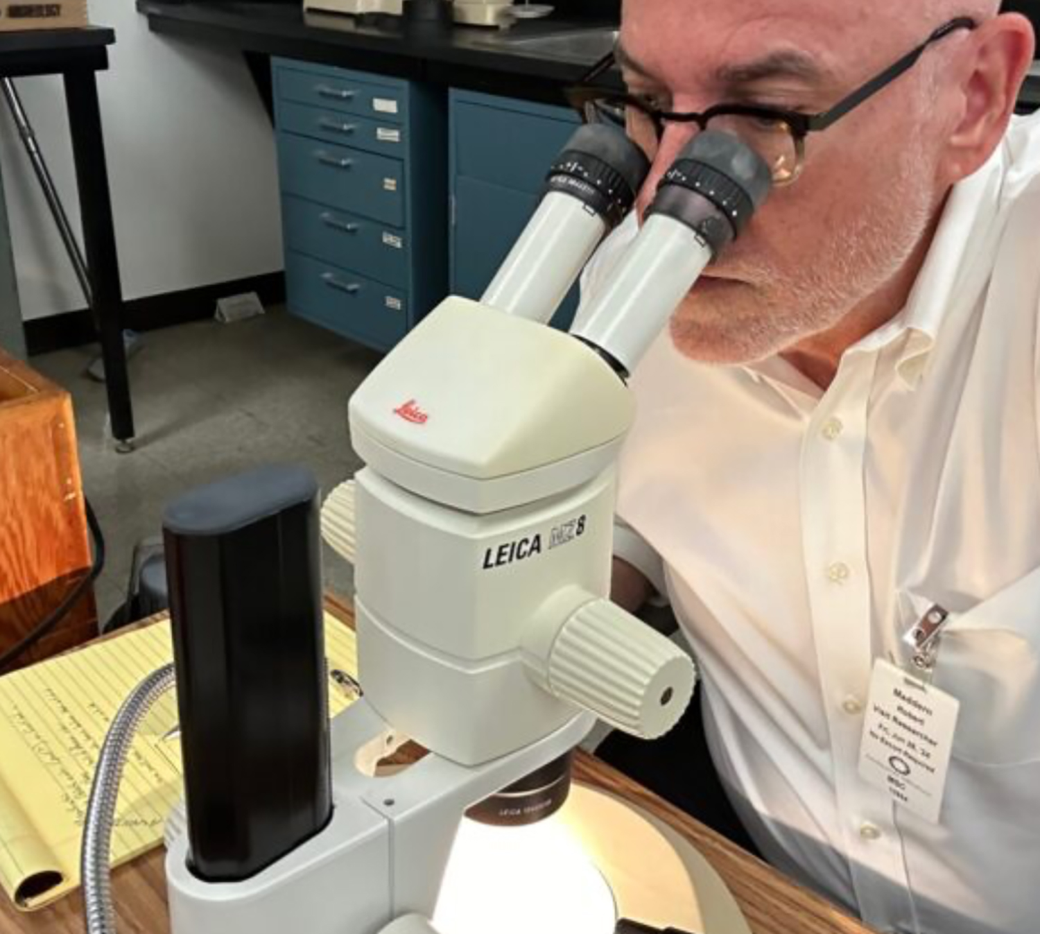 Robert Madden sits in a lab setting and looks in a microscope.
